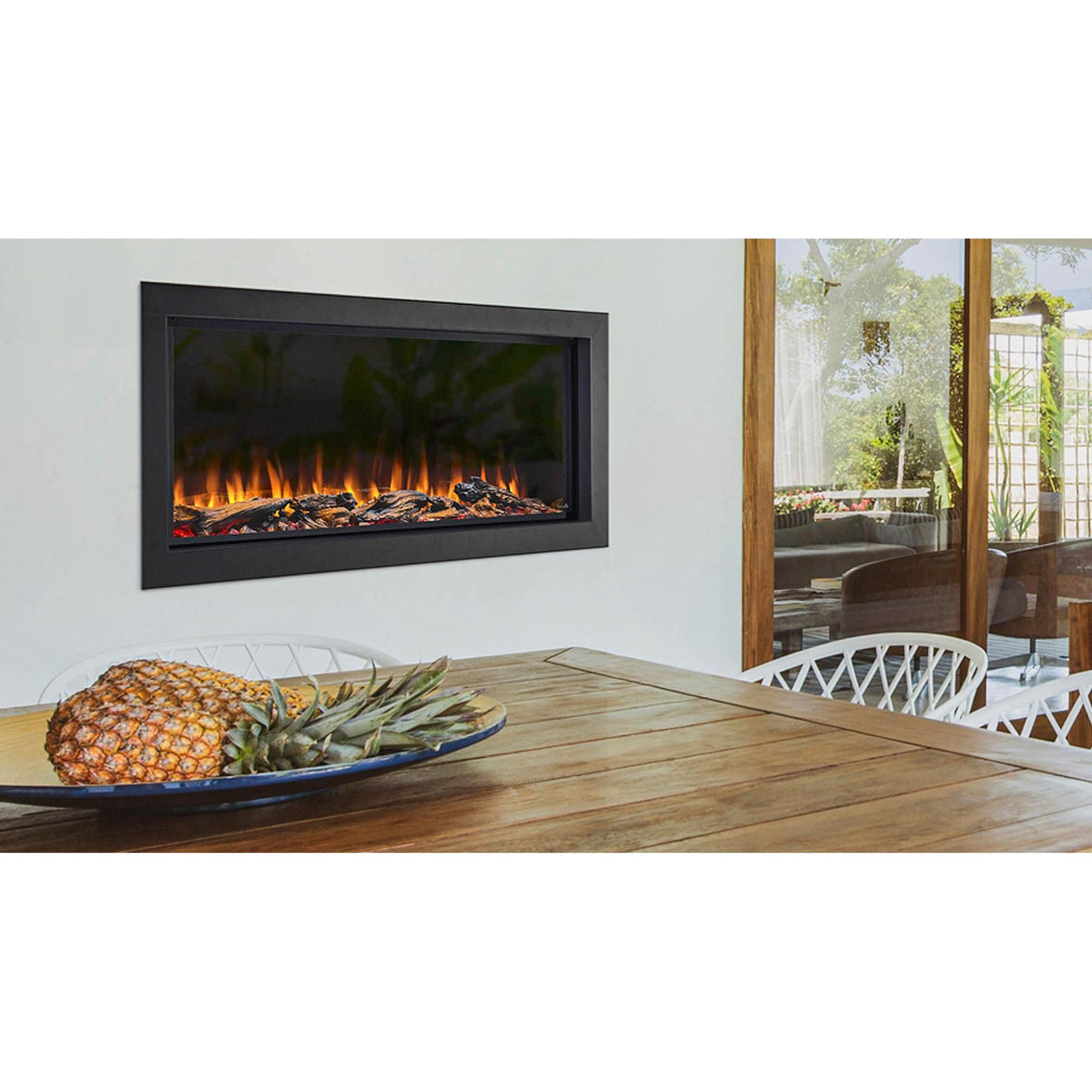 SimpliFire Forum 43: Showcasing a covered outdoor patio is a linear electric outdoor fireplace with driftwood logs with wood table nearby. Optional logs and surrounding finishes may be shown.